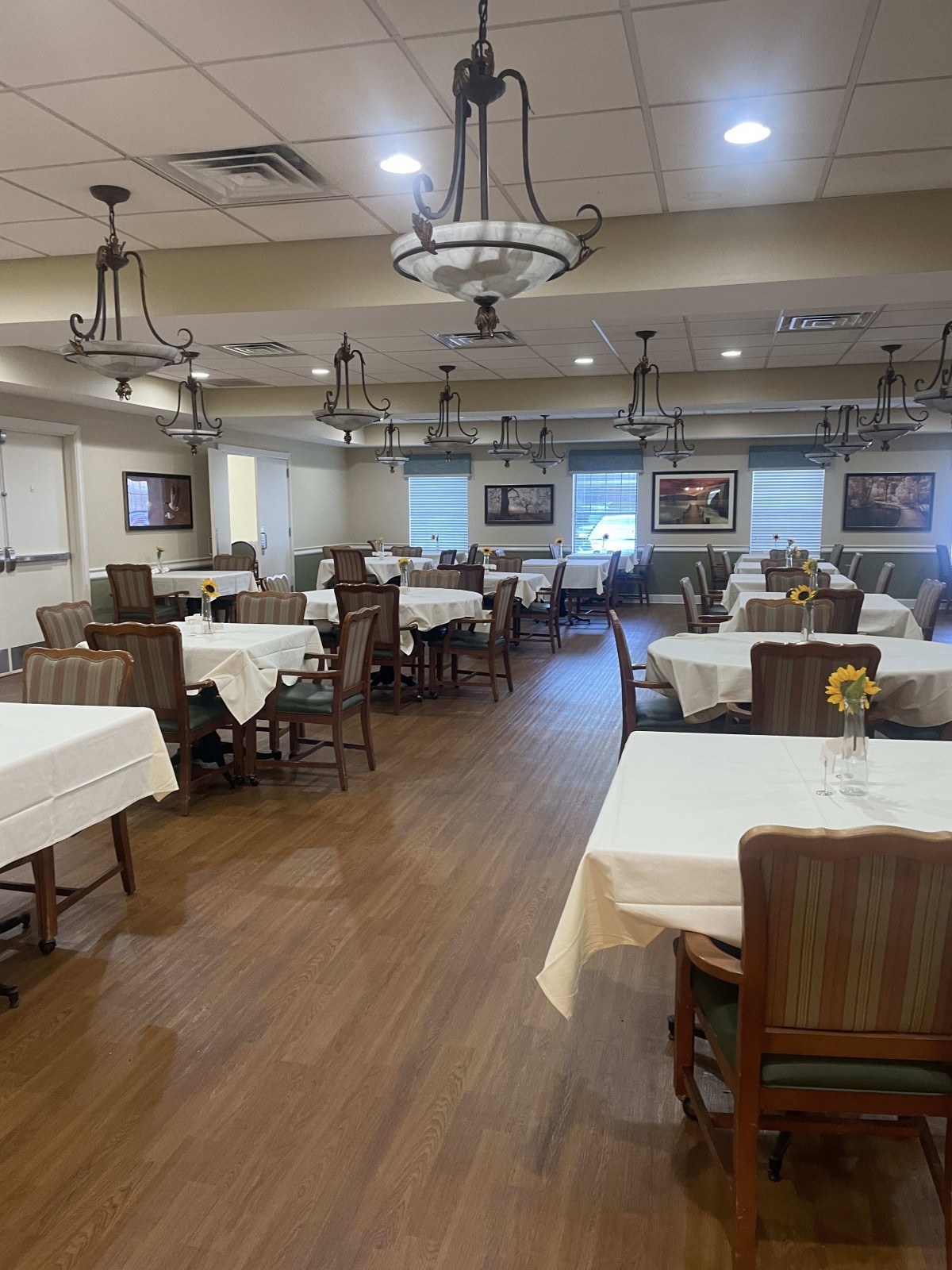 An empty dining room with set tables and wooden chairs, decorated with chandeliers.