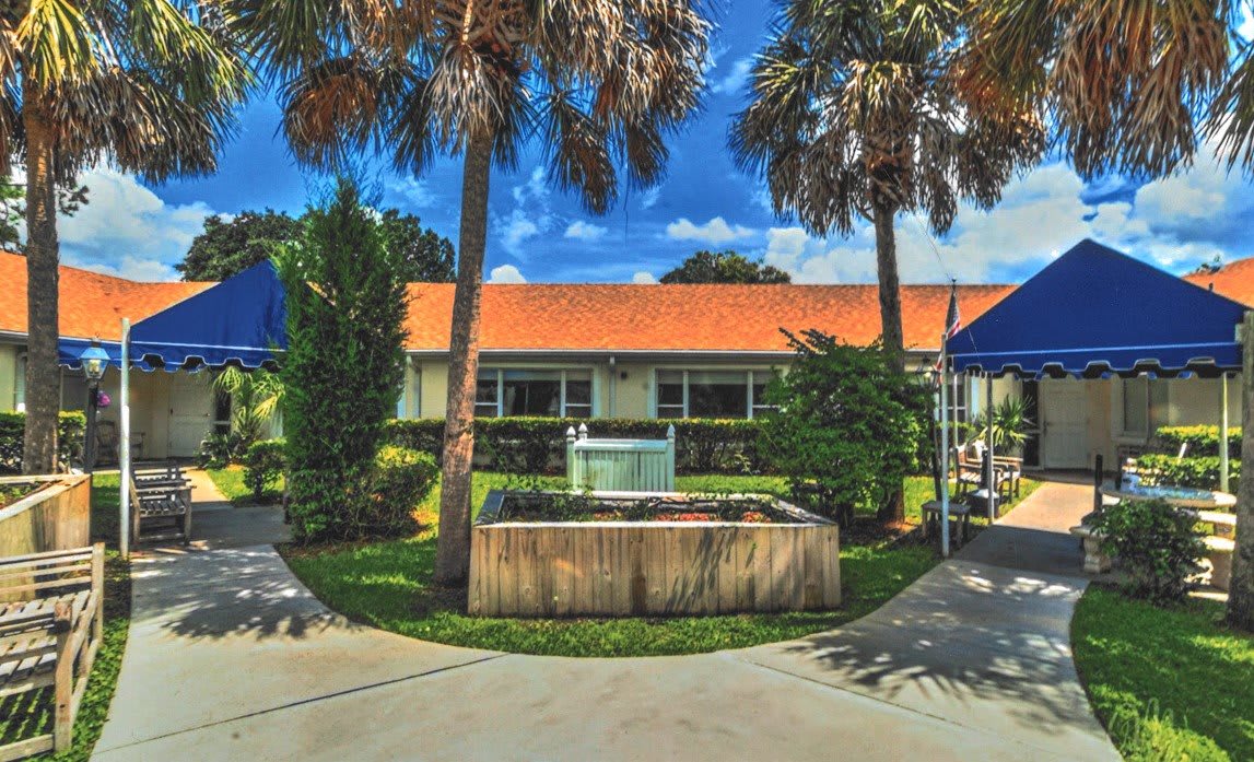 A building with a red roof surrounded by palm trees and a fountain in front.