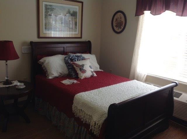 A cozy bedroom with a neatly made bed, decorated with pillows and a throw blanket, illuminated by natural light from a window.