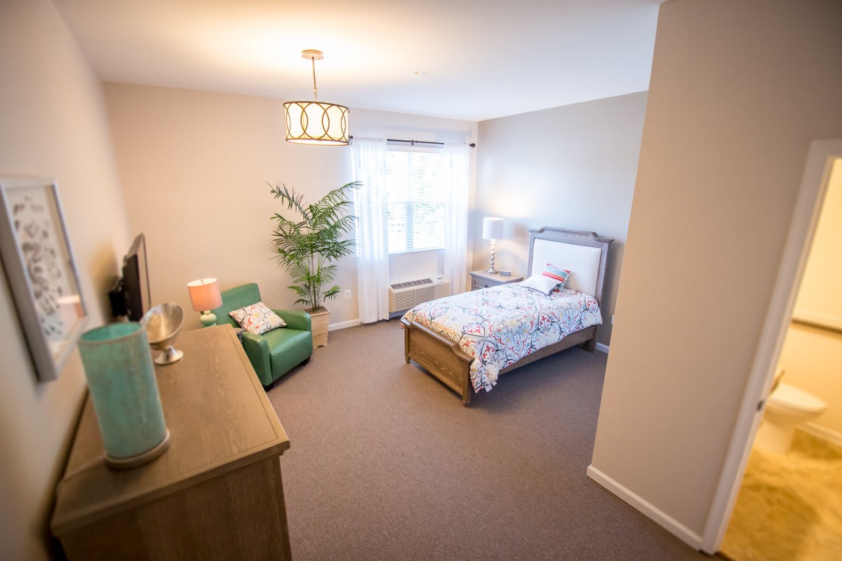 A cozy bedroom with a single bed, a green chair, and a wooden dresser.