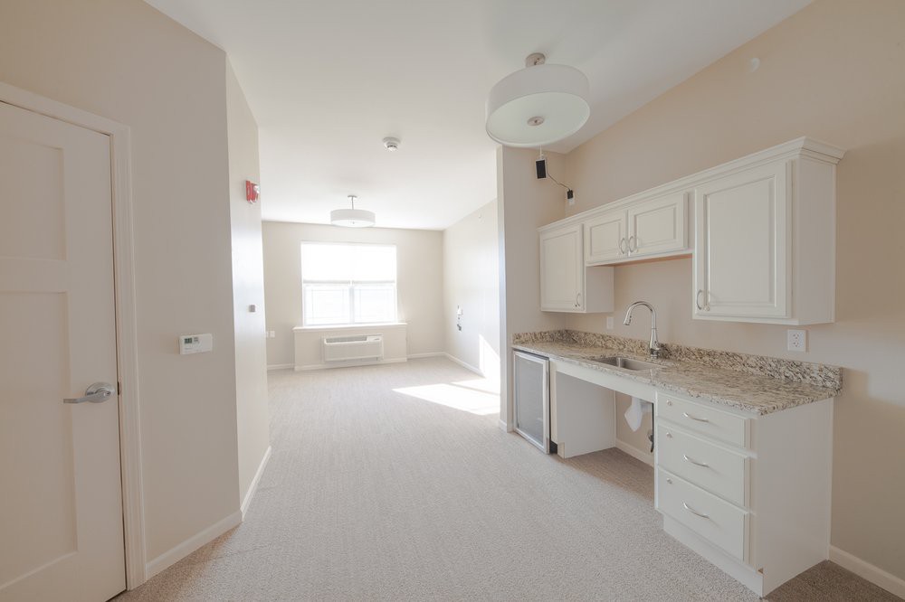 A bright and empty apartment interior featuring a small kitchen area with white cabinets.