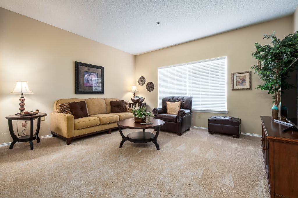 A cozy living room with a yellow sofa, brown armchair, and a central coffee table on a carpeted floor.