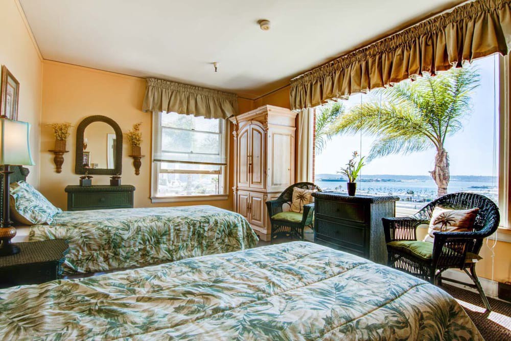 A cozy hotel room with double beds overlooking a beautiful ocean view through large windows.