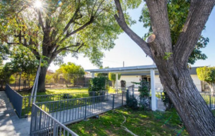 A charming house with a front porch, surrounded by a lush yard and large trees under bright sunlight.