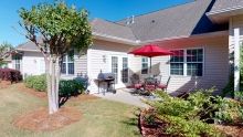 A cozy backyard patio with outdoor seating, a grill, and an umbrella on a sunny day.