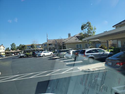 A view of a busy parking lot with various cars parked outside a building under a clear blue sky.