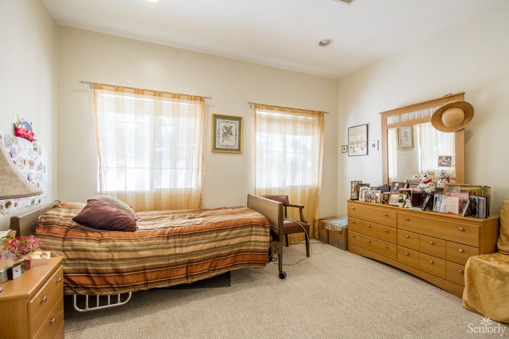A cozy bedroom with a single bed, dresser, and soft lighting from the windows.