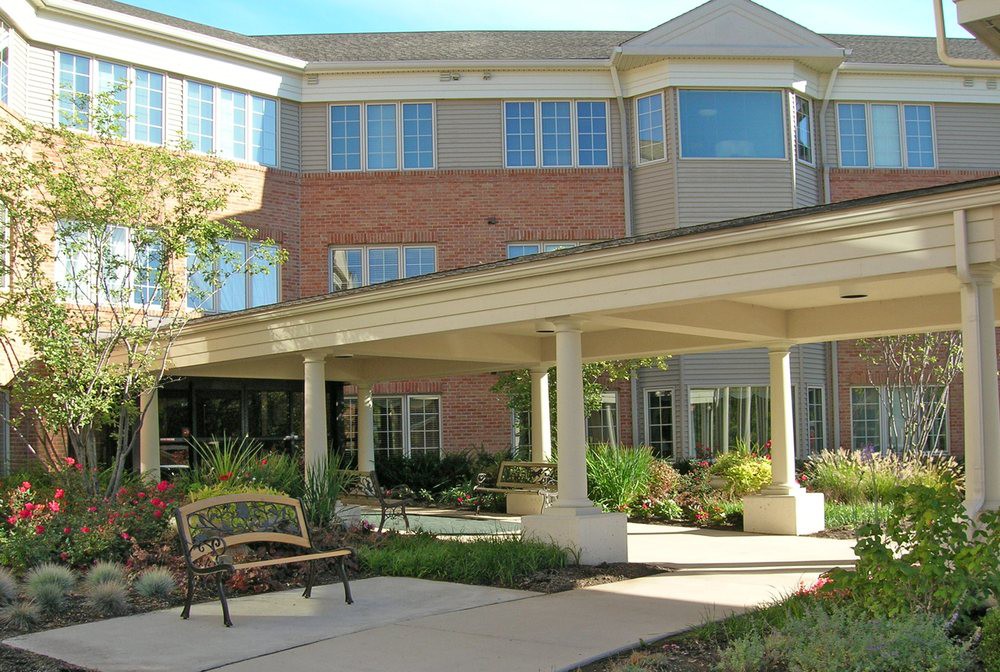 A sunny view of a residential building with landscaped greenery and an entrance canopy.