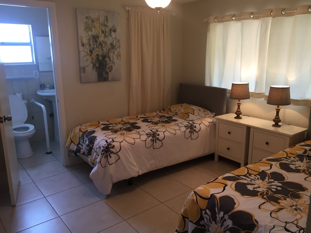 A cozy bedroom featuring two single beds with floral bedding, a nightstand with a lamp, and wall art.
