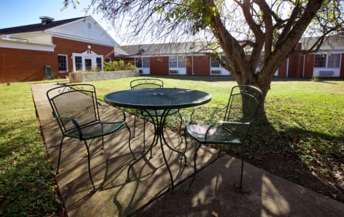 A sunlit patio area with a metal table and chairs surrounded by a garden.