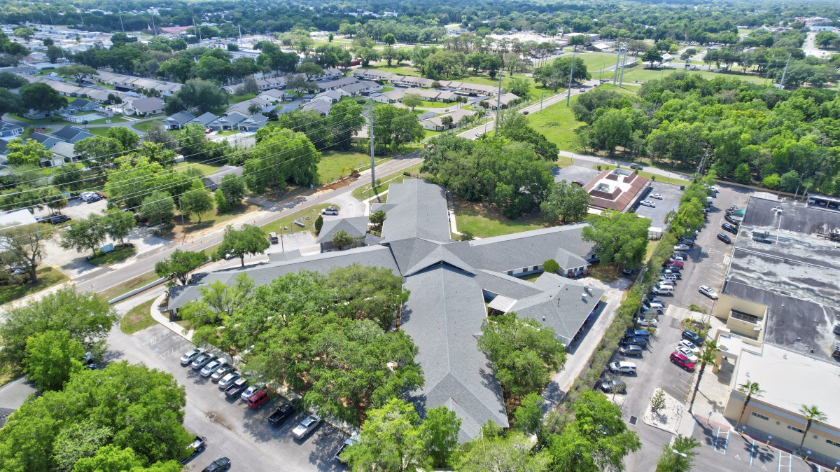 Aerial view of a large building surrounded by a parking lot and greenery.