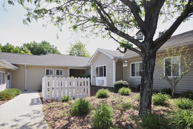 A well-maintained single-story house with a fenced front yard, surrounded by trees and landscaped garden.