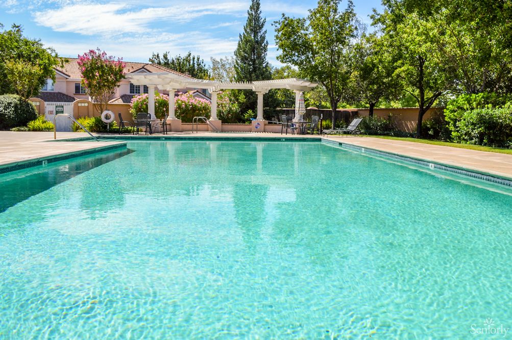 A serene outdoor swimming pool surrounded by lush greenery and a patio area.