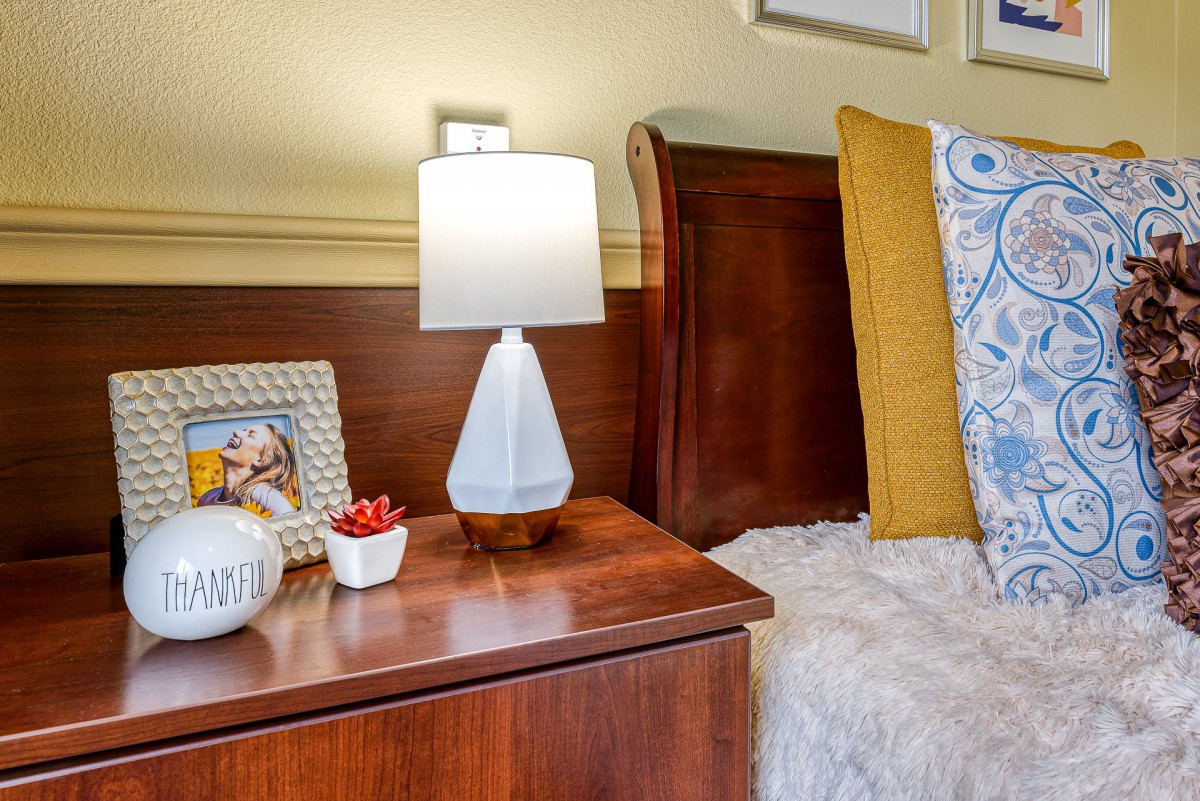 A cozy bedroom scene featuring a wooden nightstand with a stylish lamp, decorative items, and plush bedding.