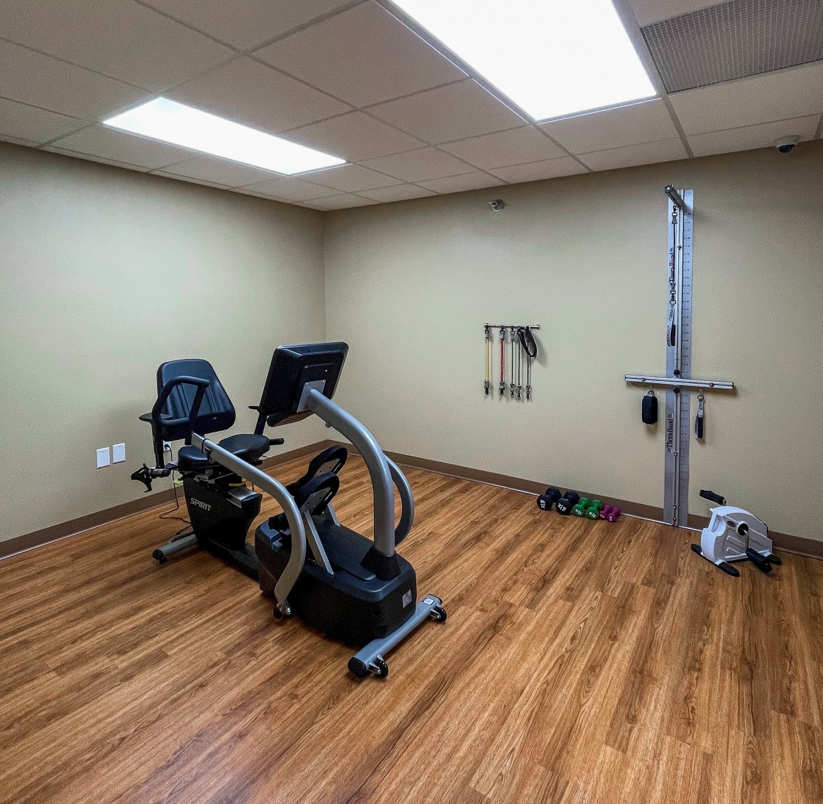 A small gym room featuring an exercise bike and fitness equipment on a wooden floor.