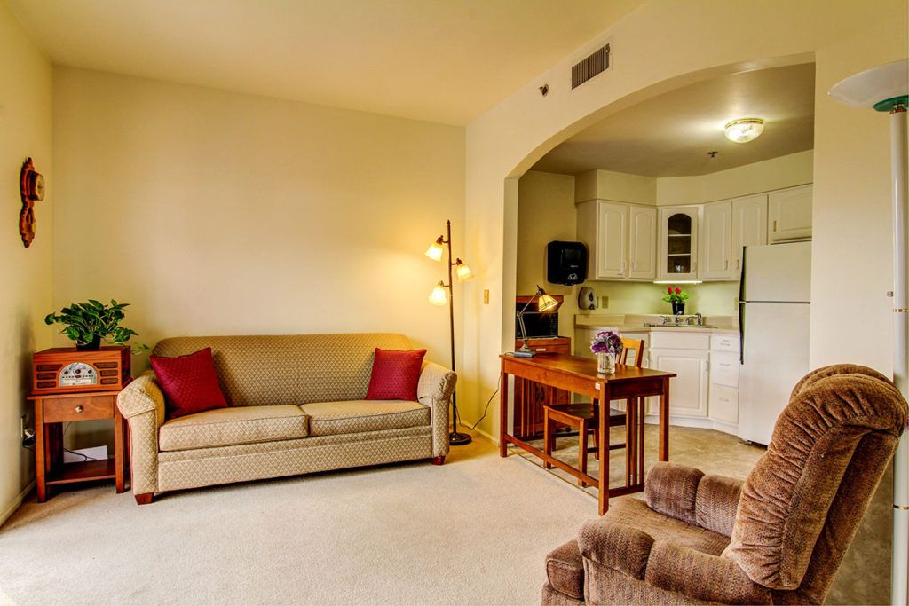 A cozy living room with a view of the kitchen, featuring comfortable seating and warm lighting.