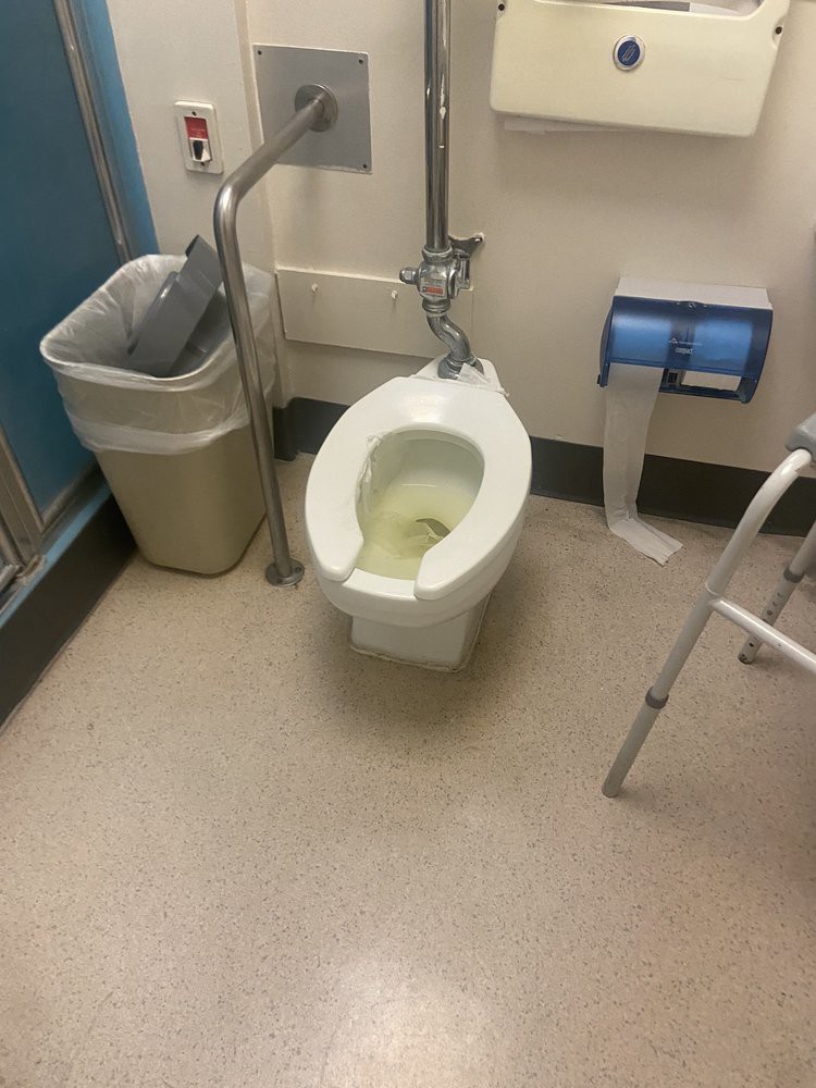 A bathroom with a toilet, trash can, walker, and toilet paper holder.