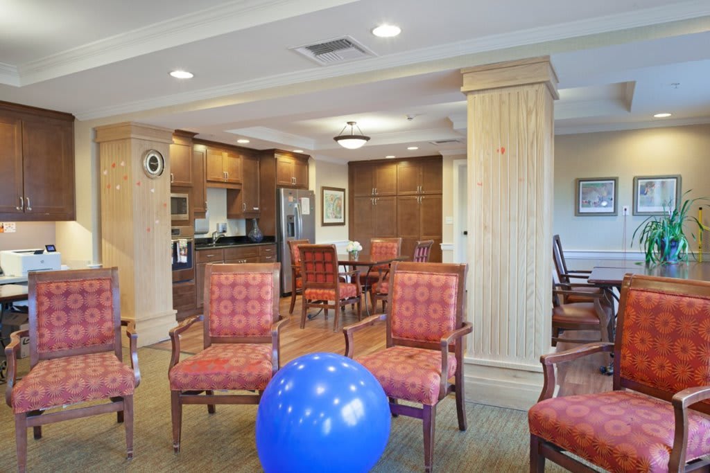 The image shows a furnished room with chairs, a table, and a kitchen area, featuring a blue exercise ball in the center.