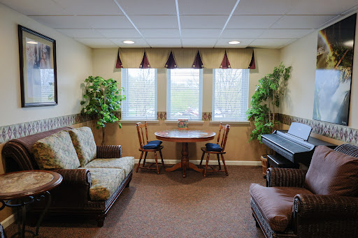 A cozy living room setup featuring a sofa, a small dining table with chairs, and a piano, complemented by some indoor plants.