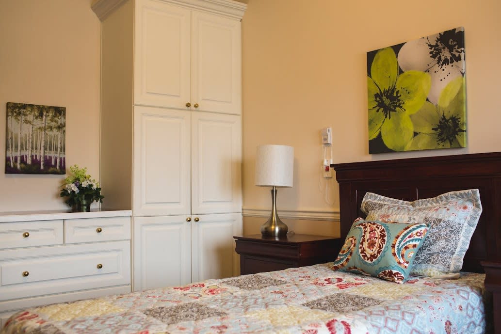 A cozy bedroom featuring a large wardrobe and bedside table with a lamp, complemented by colorful pillows on the bed.