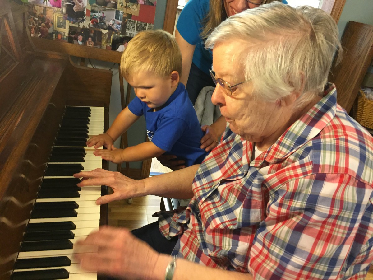 An elderly person and a child playing the piano together, sharing a musical moment.