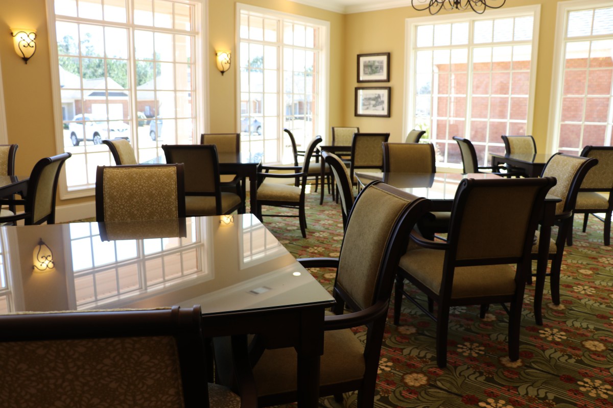 A sunlit dining room with tables and chairs arranged neatly by the windows.