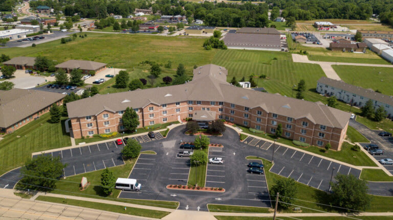 Aerial view of a large building with a parking lot and surrounding greenery.