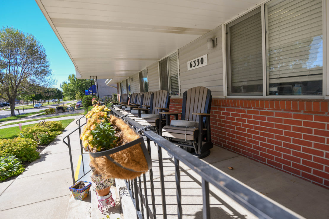 A row of rocking chairs on a porch with hanging flower baskets.