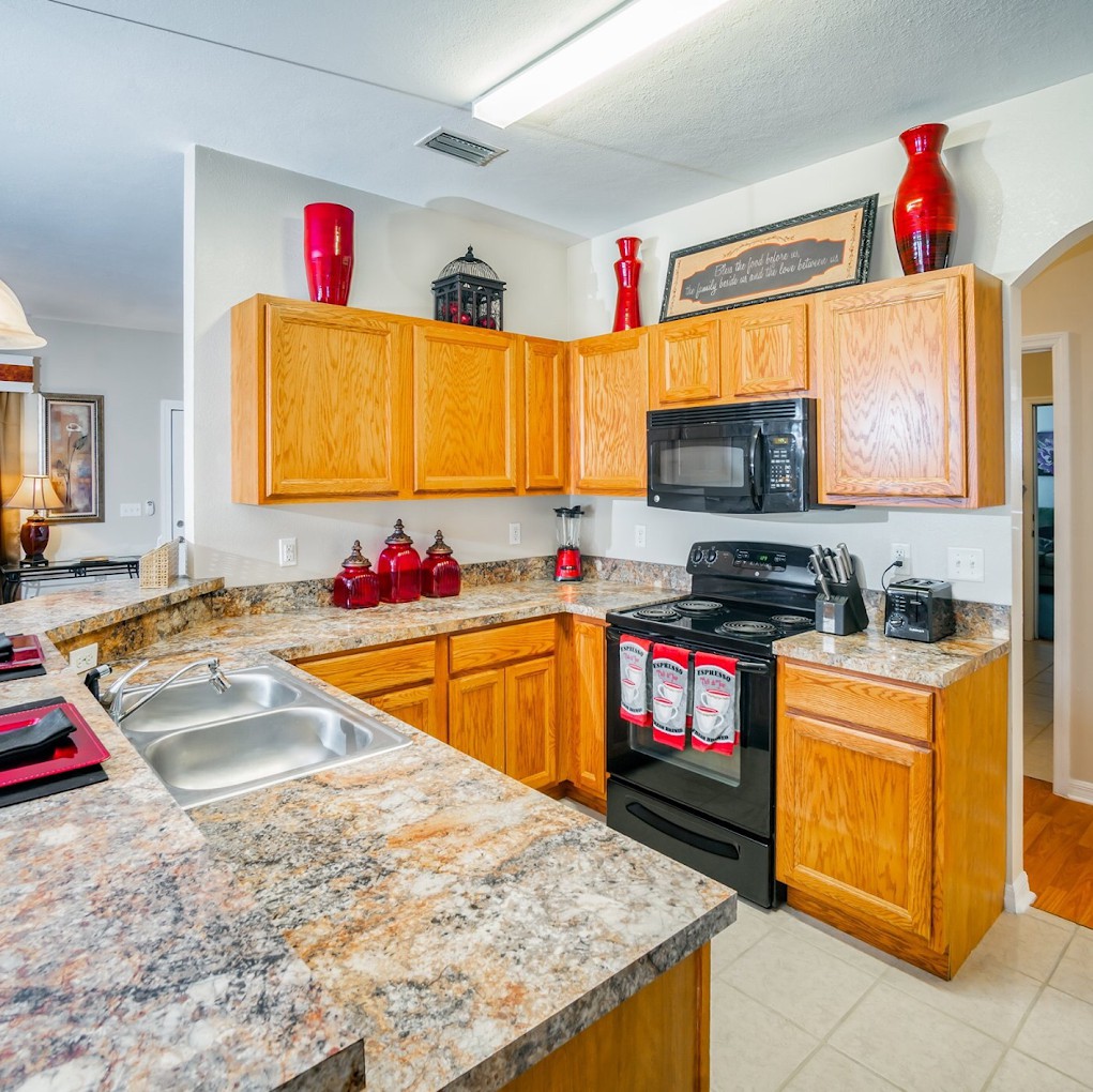 A modern kitchen with wooden cabinets, granite countertops, and red decorative accents.