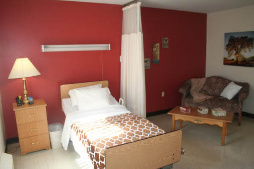 A simple hospital room featuring a single bed, a chair, and red walls.