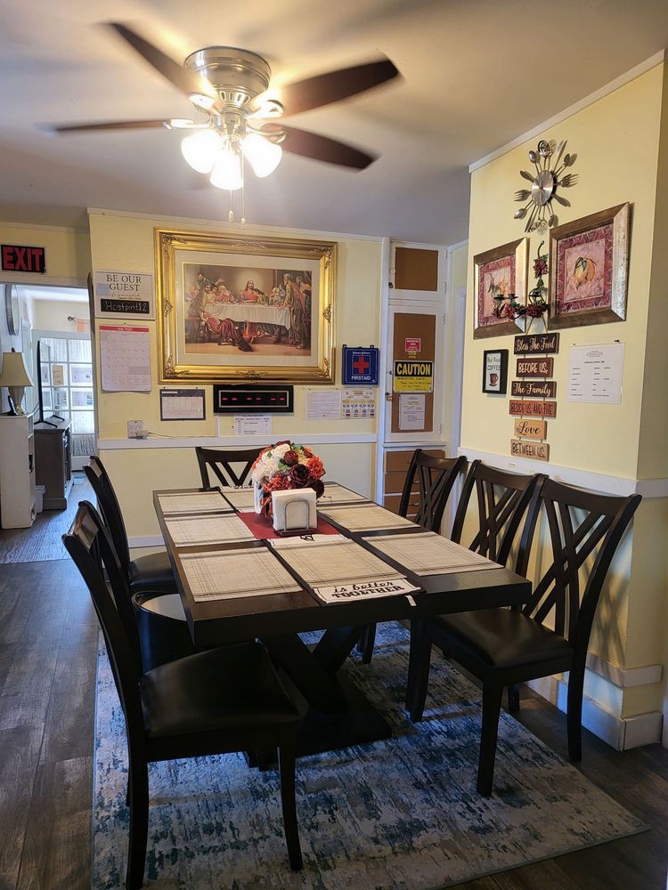 A cozy dining area featuring a large table with chairs, decorated walls with artwork and family photos, under a ceiling fan.