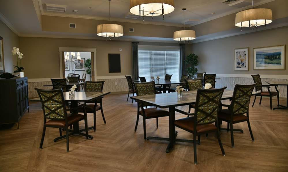 A quiet dining room with neatly arranged tables and chairs, illuminated by stylish overhead lighting.