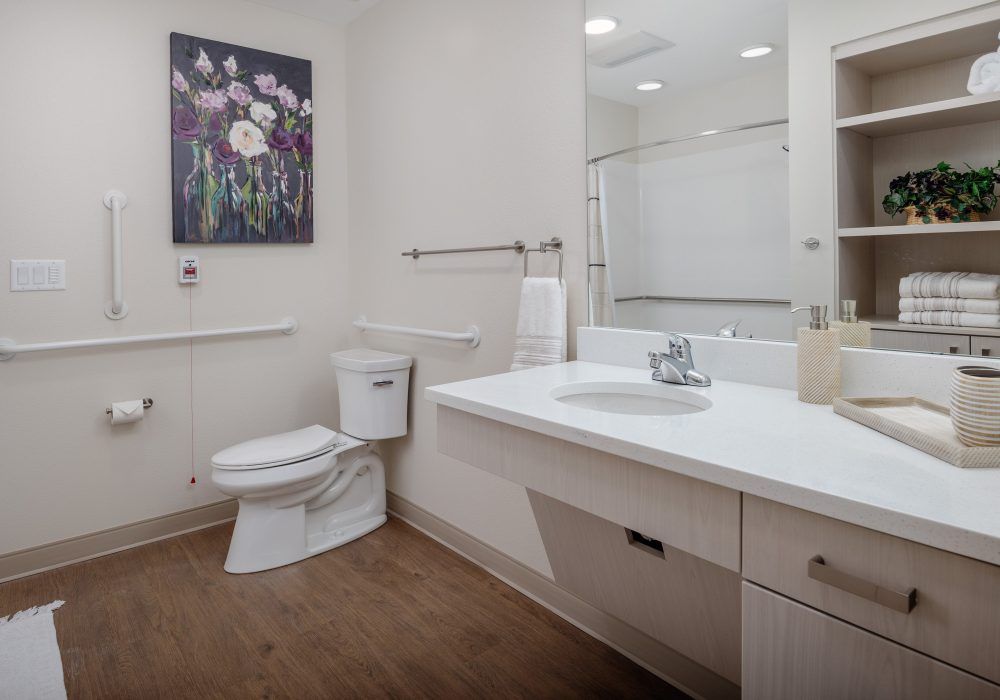 A clean and modern bathroom featuring a large sink area, toilet, and shower, with decorative artwork on the wall.