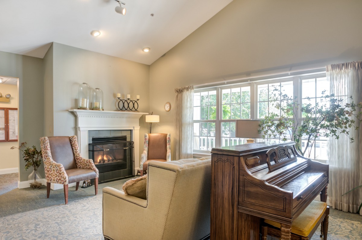 A cozy living room featuring a fireplace and a piano, with ample natural light streaming in through large windows.