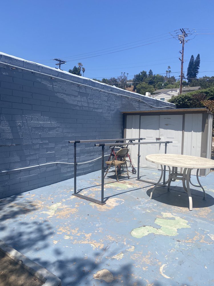 A sunny outdoor patio with a round table and some chairs, set against a painted wall.