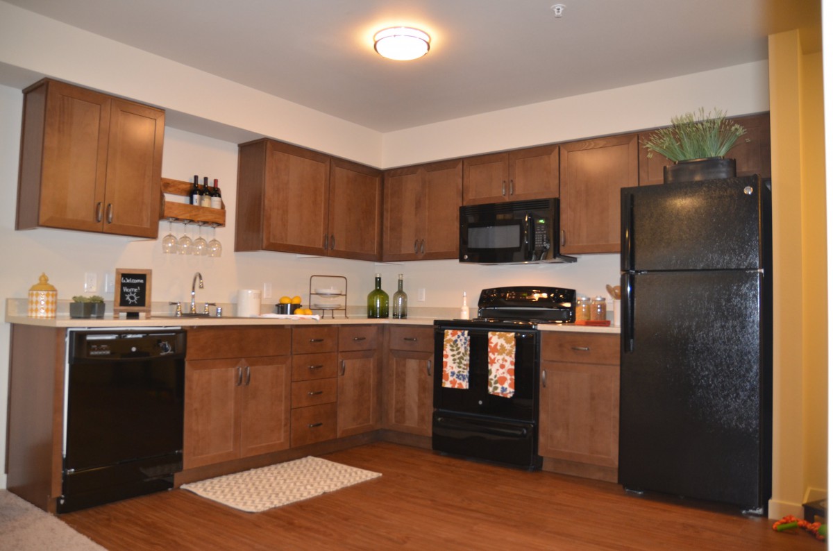 A modern kitchen with wood cabinets and black appliances.