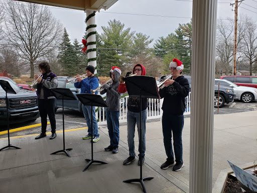 A group of musicians performing holiday tunes outdoors, dressed in Santa hats.