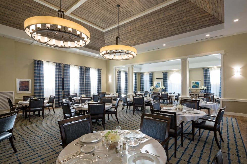 An elegant dining room with neatly arranged tables and chairs, illuminated by chandeliers.