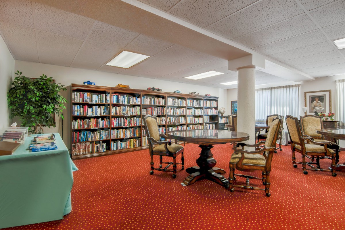 A cozy library space with bookshelves, a table, and chairs on a red carpet.