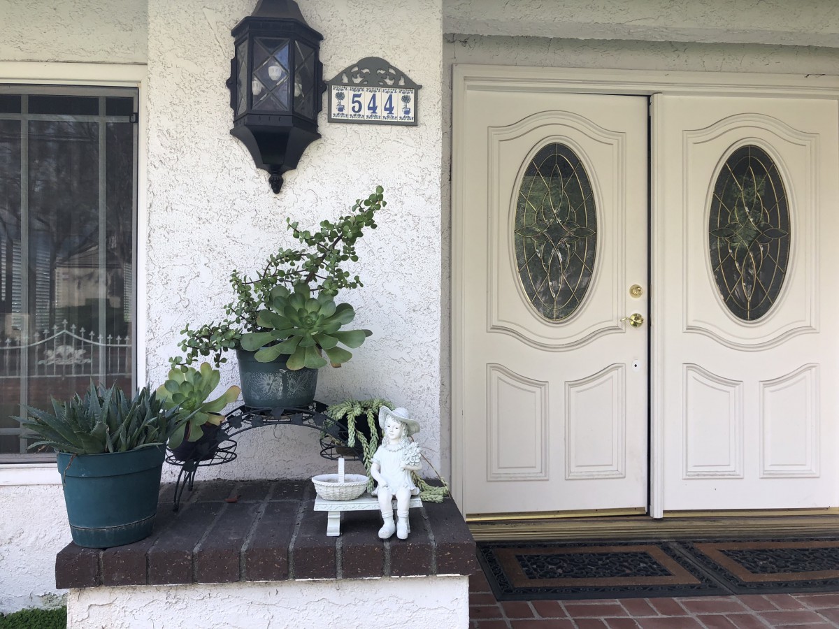 A welcoming front porch with double doors, adorned with plants and a small statue under a traditional lantern.