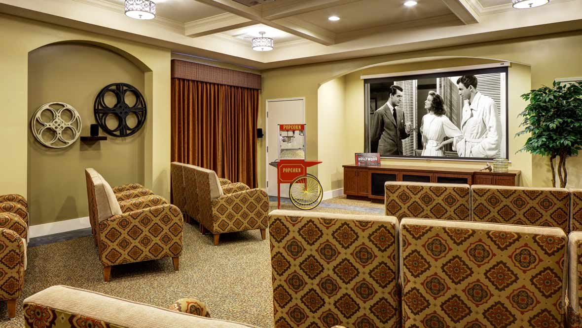 A cozy home theater setup with plush seating and a large projector screen displaying a black and white movie.