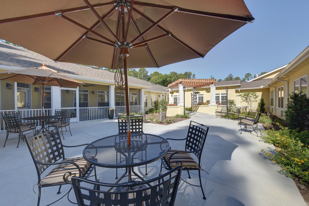 A sunny patio with metal chairs and an umbrella-shaded table in a residential area.
