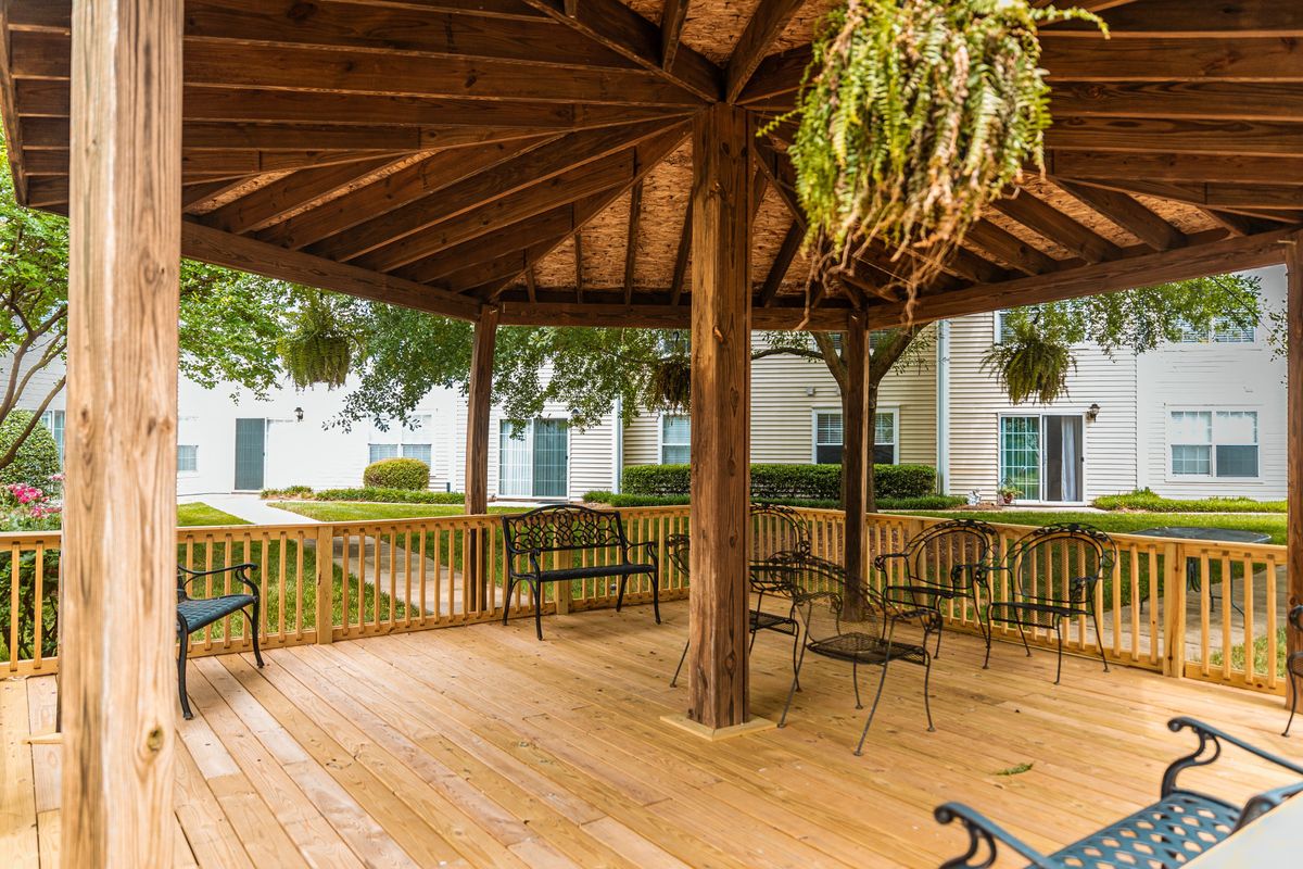 A wooden gazebo with outdoor seating and hanging plants in a garden setting.