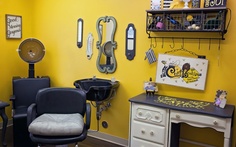 A vibrant hair salon with yellow walls and stylish decor, featuring a salon chair and wash station.