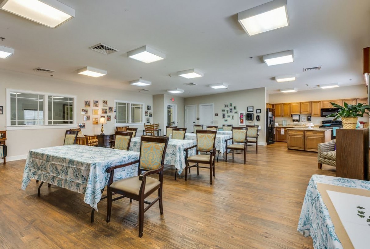 A spacious dining area with multiple tables and chairs, featuring a community kitchen.