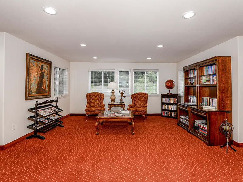 A cozy living room with red carpet, featuring elegant armchairs and well-stocked bookshelves.