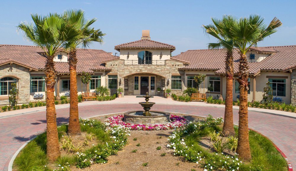 A luxurious Mediterranean-style mansion with a fountain and palm trees in the front yard.