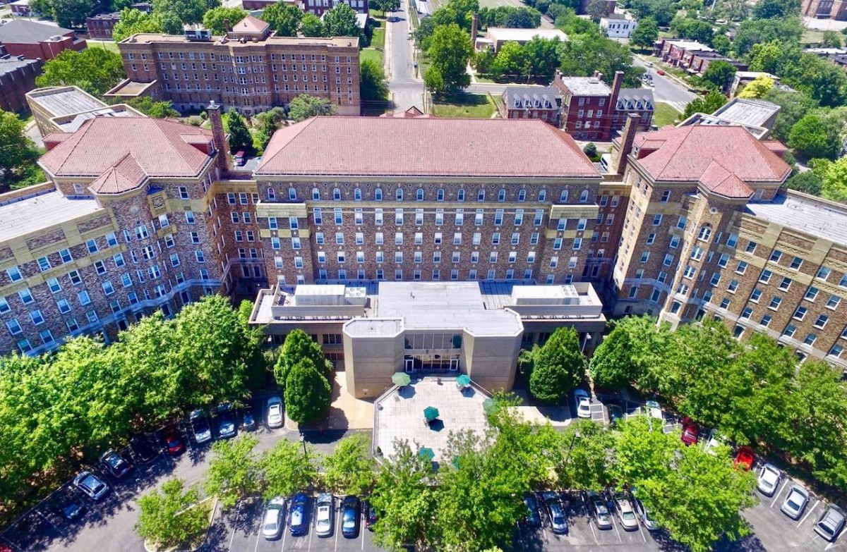 Aerial view of a large building with surrounding greenery and parking areas.