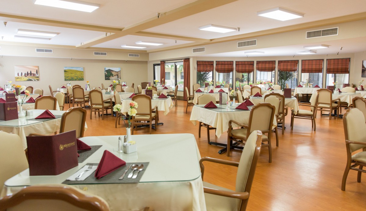 An elegant dining room with neatly arranged tables and chairs, featuring folded napkins and a warm, inviting atmosphere.