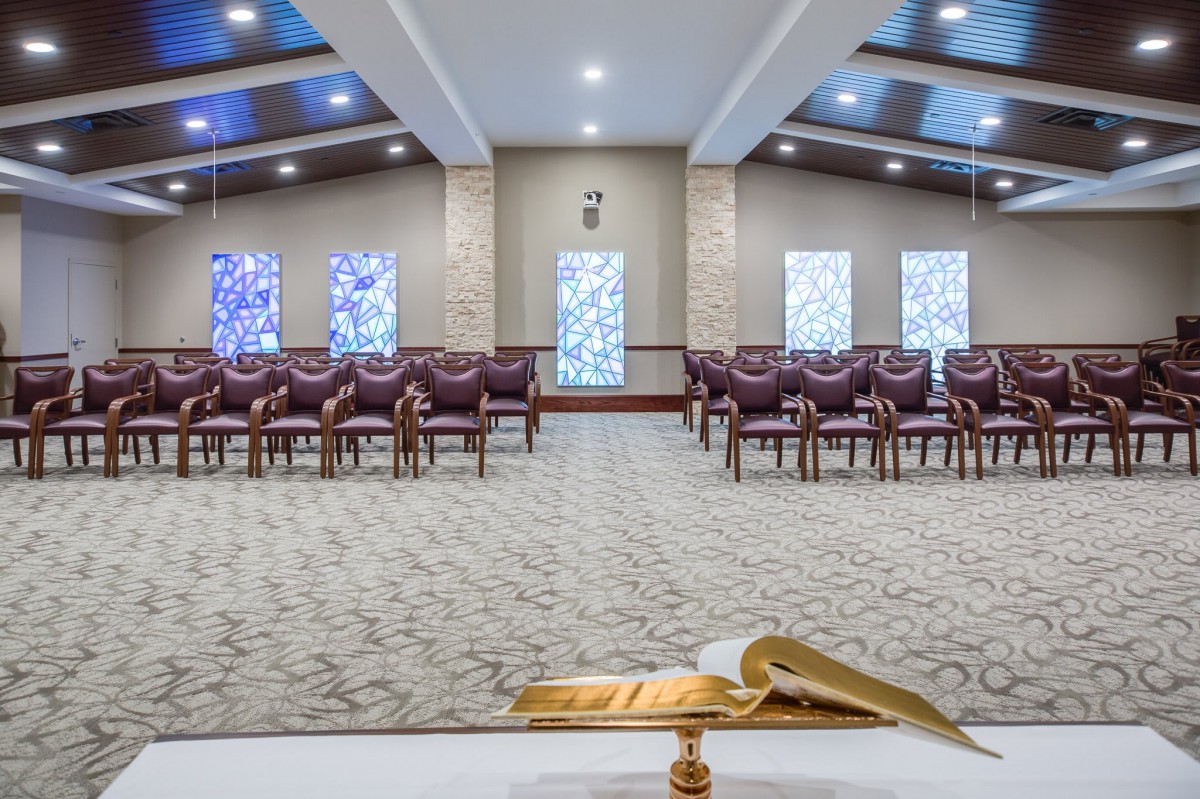 A serene chapel interior featuring stained glass windows and rows of seating, viewed from behind a pulpit with an open book.